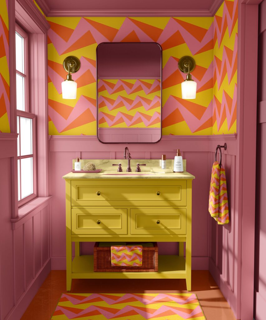 Bathrom in soft pink with a bold yellow pink orange 3D zigzag pattern on a wallpaper and the same pattern on the towels and the rug.