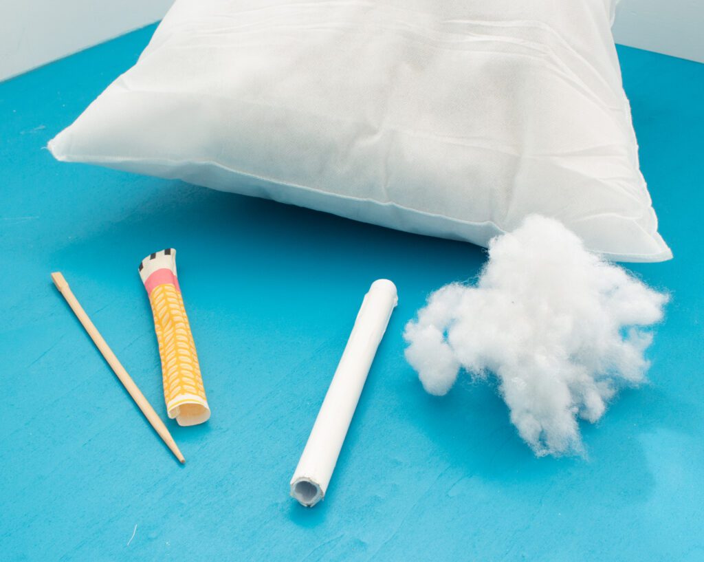 Pillow with filling fibre, a chopstick, a paper roll and a fabric leg of a stuffed animal laying on a table