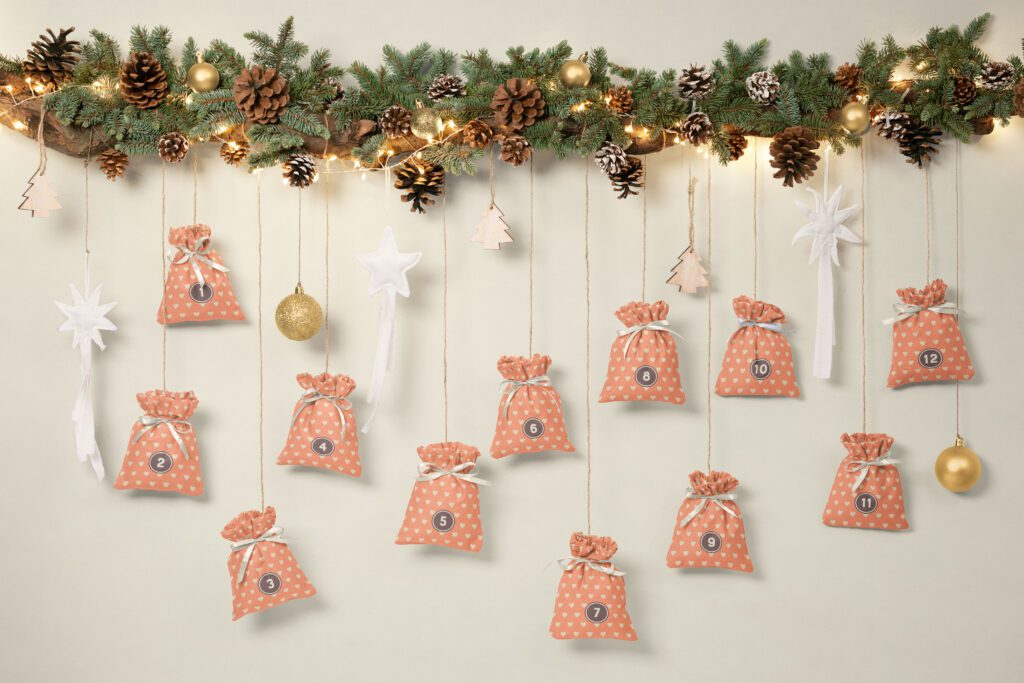 Kitschy peach orange Advent calendar bags with cream white hearts hanging down some Christmas-y decorated branches on a beige white wall