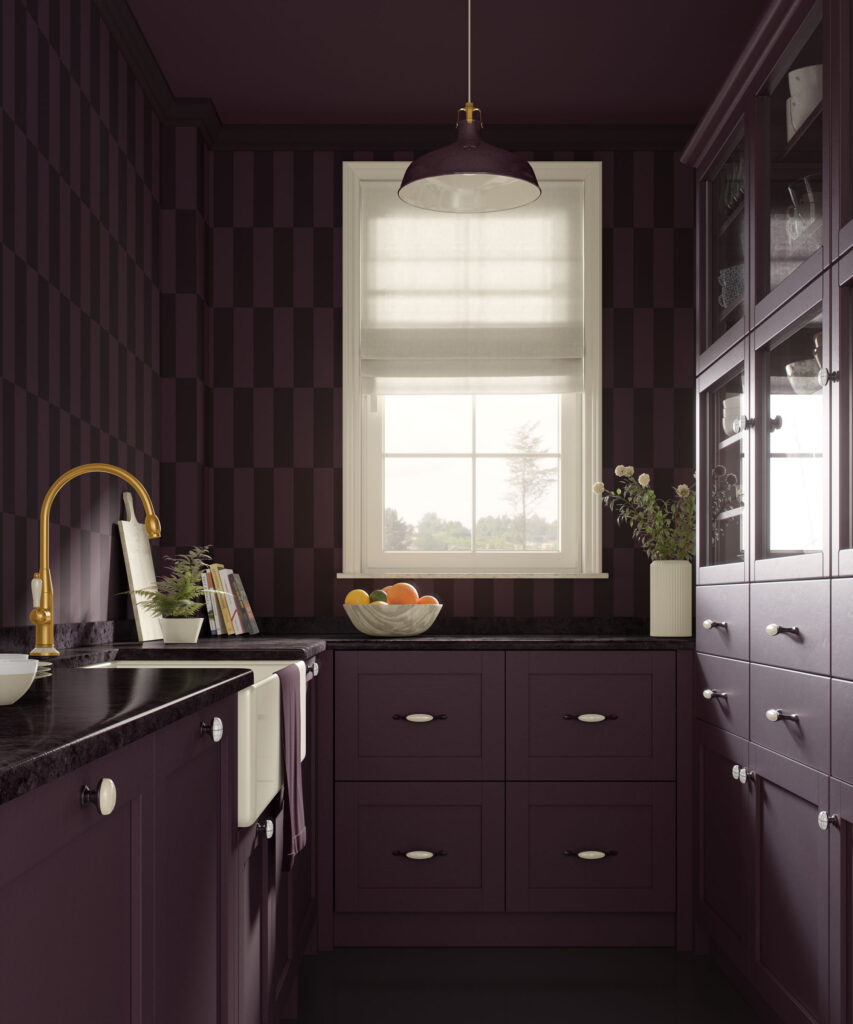 Dark plum and blackish striped traditional non-pasted wallpaper in a small modern kitchen with matching plum shaker cabinets, black countertops, brass faucet, white farmhouse sink, fruit bowl, and a single window with a white roman shade.