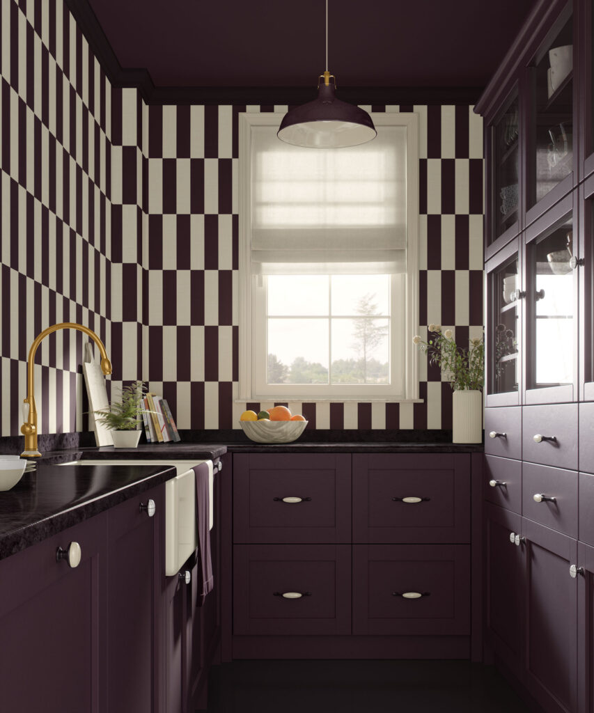 Dark plum and beige linen-textured vertical stripe wallpaper in a modern kitchen with matching plum cabinets, black countertops, brass faucet, white farmhouse sink, glass-front pantry cabinet, white Roman shade, and a bowl of fruit on the counter under a dark pendant light.