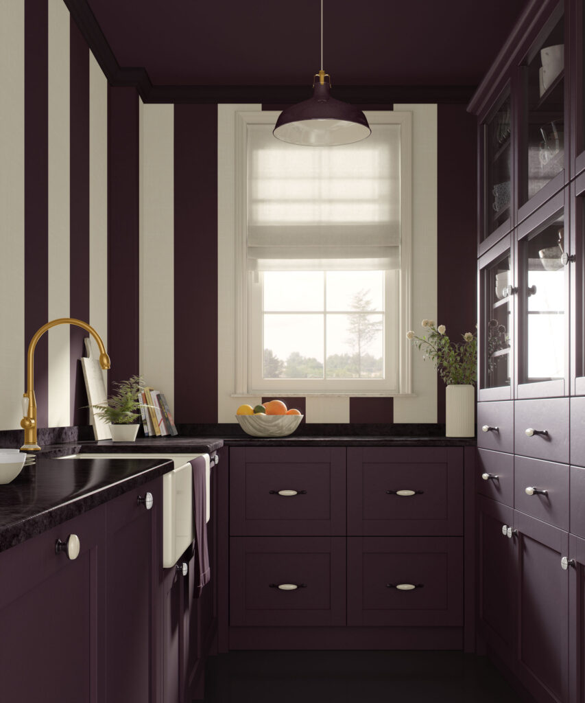Dark plum and beige vertical striped traditional non-pasted wallpaper in a small kitchen, with matching plum shaker cabinets, black countertops, a brass faucet, a window with a white roman shade, and a dark plum painted ceiling under a simple pendant light.
