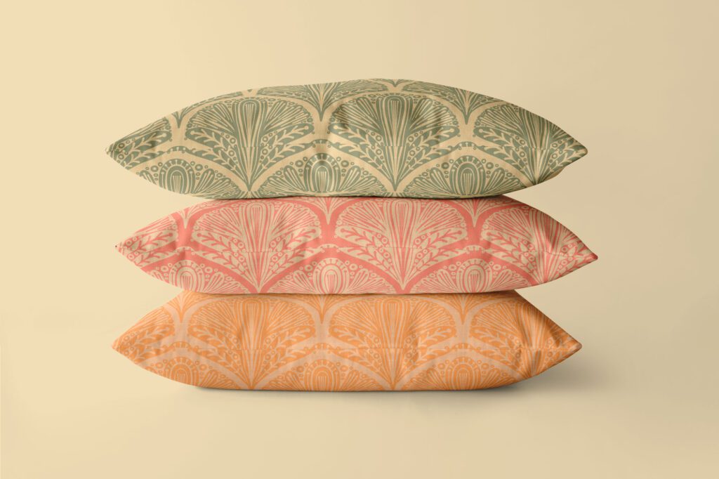 Stacked pillows featuring Art Deco print in soft orange, sage green, and muted grayish-green. The abstract floral pattern is set against a neutral background with smooth fabric textures. 