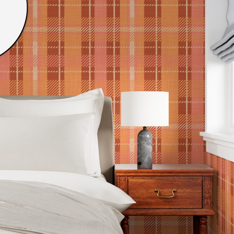 Plaid linen-textured wallpaper in warm terracotta orange, brown, coral, and vivid tangerine tones displayed in a bedroom with a white pillow, beige bedding, wooden nightstand, and dark marble table lamp.