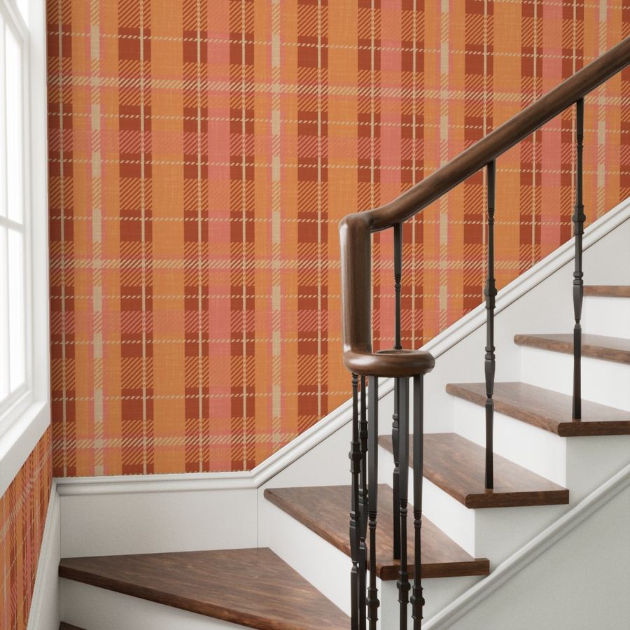 Plaid peel and stick wallpaper in warm terracotta orange, brown, coral, and vivid tangerine tones, applied on staircase walls with white trim and wooden steps with dark railings.